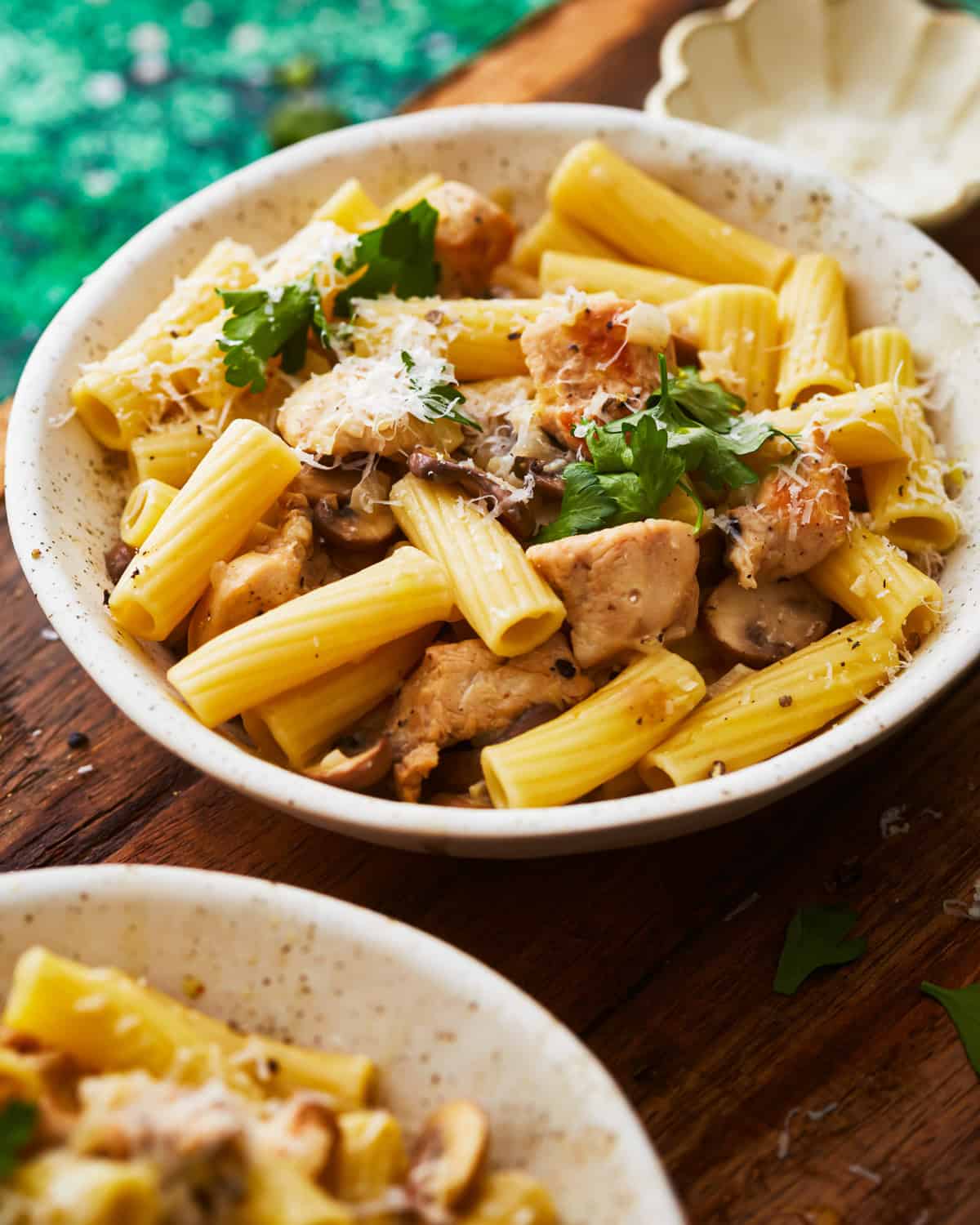 side view of a serving of chicken mushroom pasta in a white bowl with a fork.