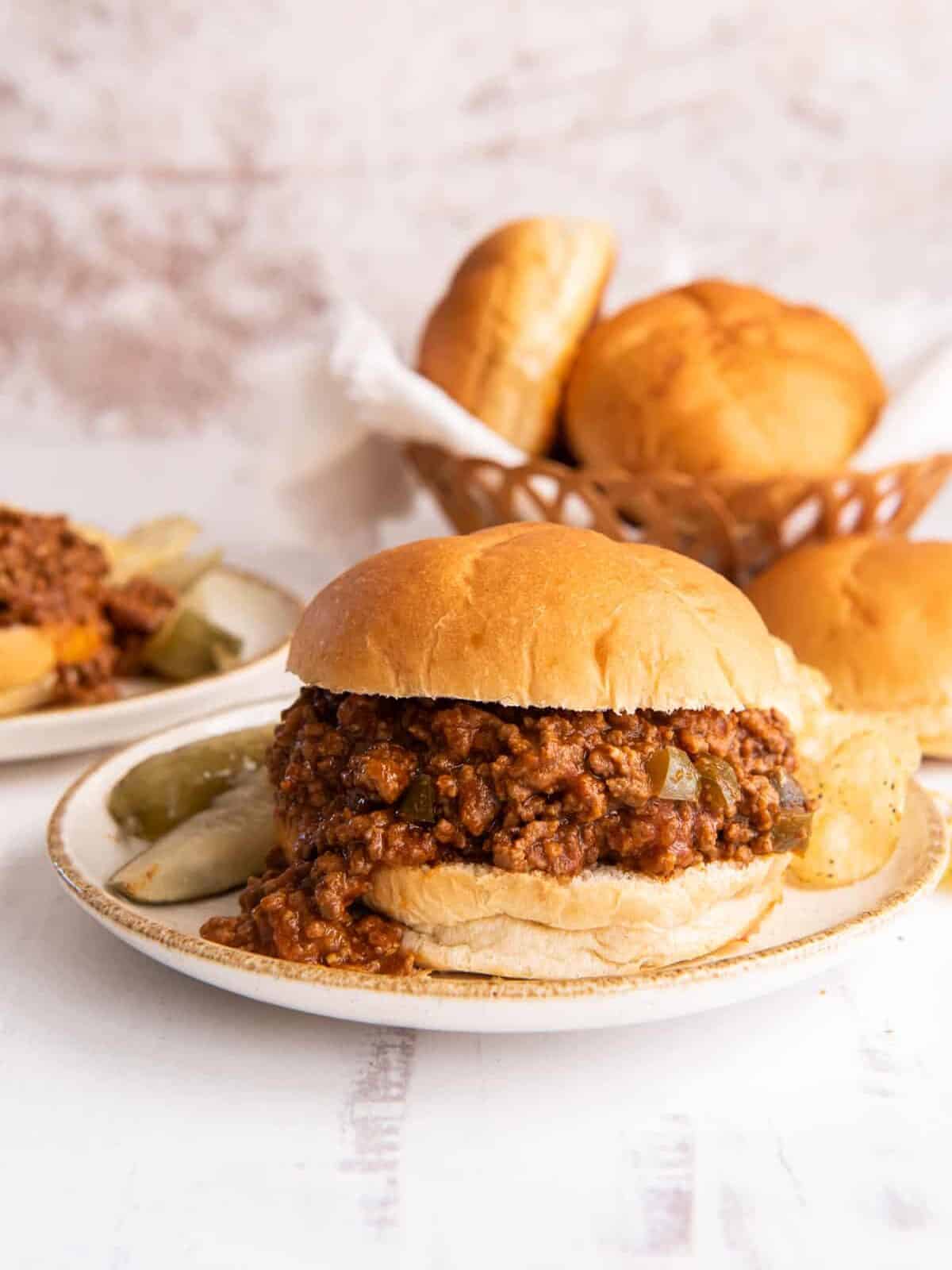 sloppy joe sandwich on a plate with chips and a pickle.