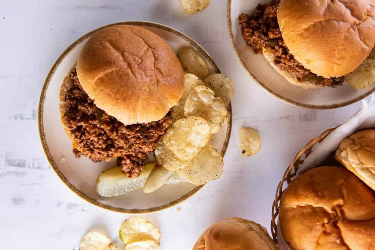 overhead view of plates of sloppy joes with potato chips and pickles.