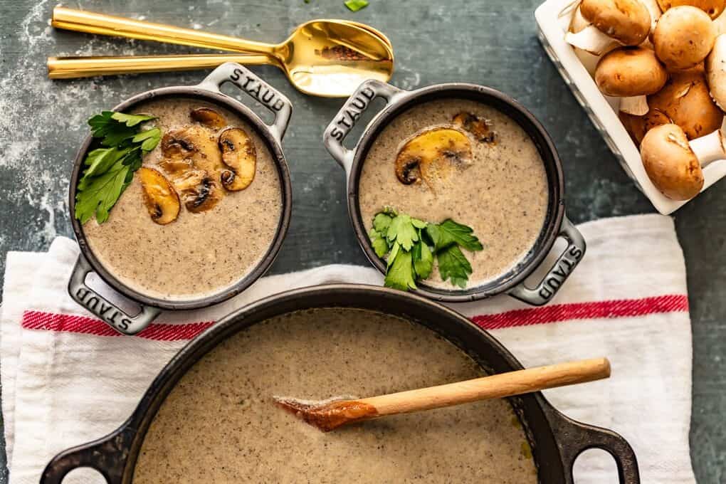 A pot of homemade cream of mushroom soup next to two bowls of it