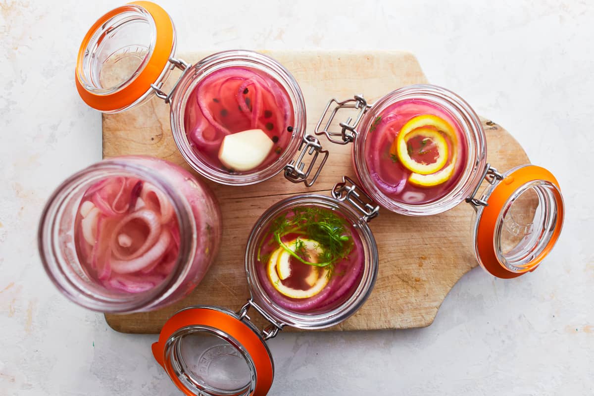 flavor variations of pickled red onions in glass jars on a cutting board.