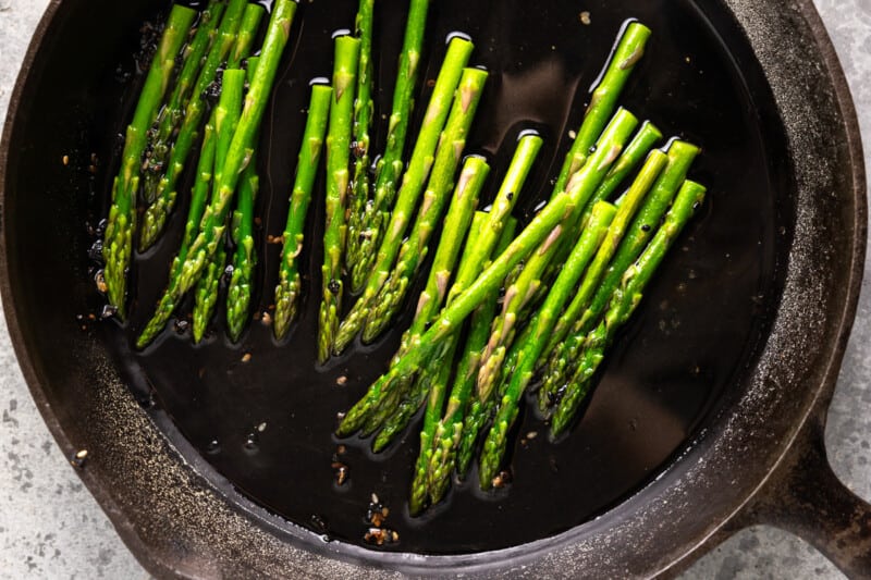 stalks of asparagus cooking in a pan of oil.