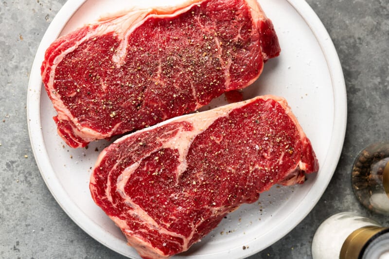 two uncooked, seasoned steaks on a plate.