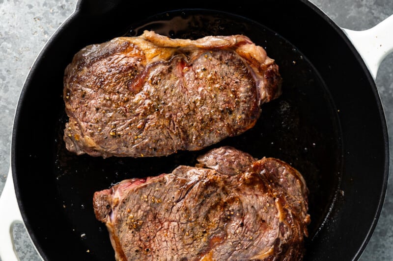 two steaks cooking in a pan.