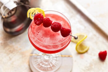 overhead view of a raspberry martini, garnished with a skewer of raspberries and a curl of lemon peel.