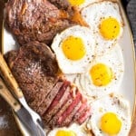 A platter of steaks and fried eggs.