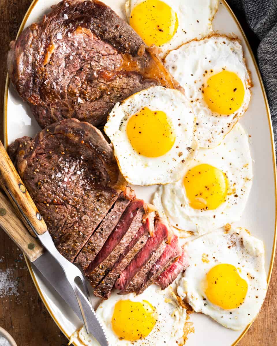 A platter of steaks and fried eggs.