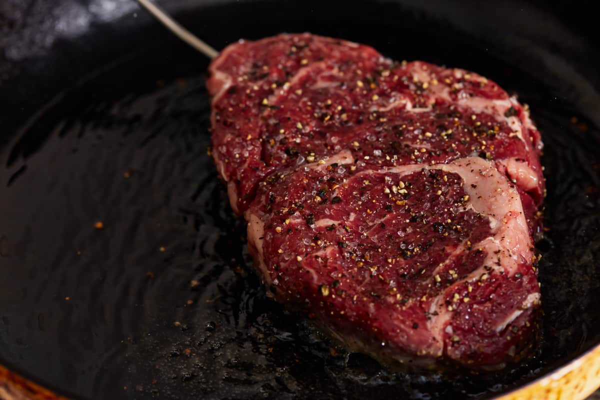 raw seasoned ribeye steak in a cast iron pan.