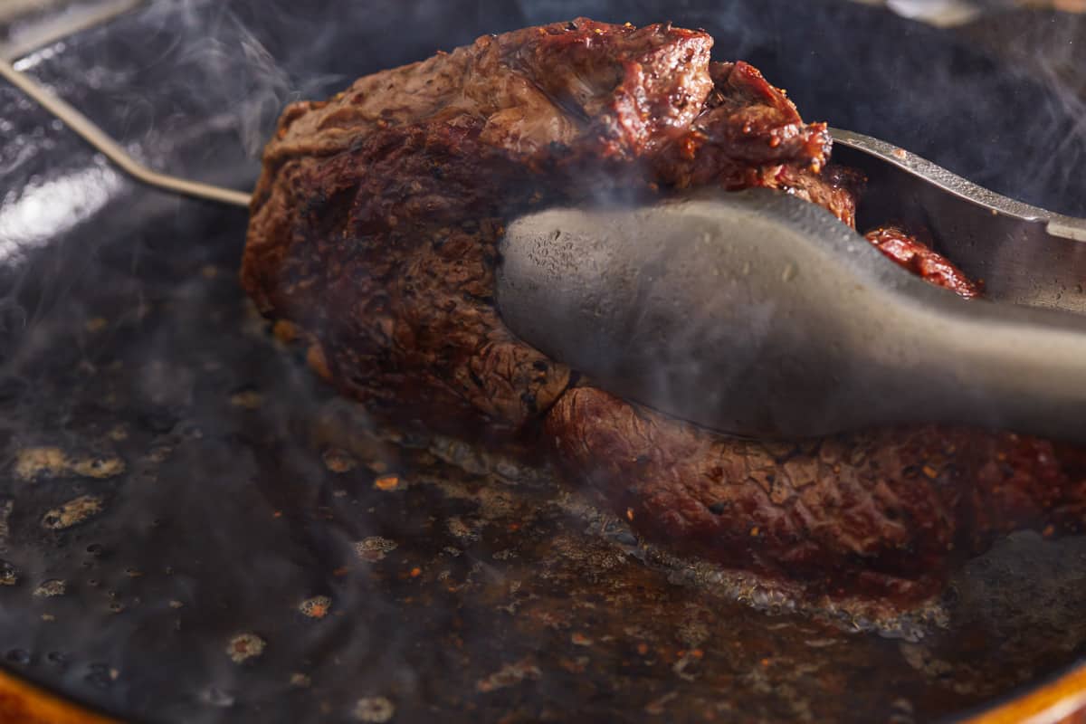 searing the edges of a steak in a cast iron pan.