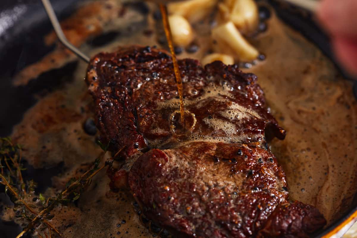 spooning butter over steak in a cast iron pan.