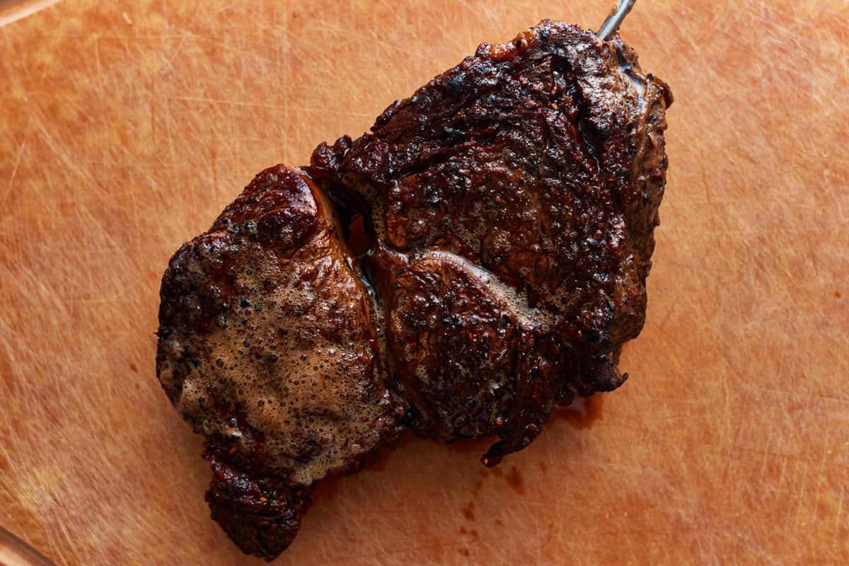 seared ribeye steak resting on a cutting board with a temperature probe sticking out.