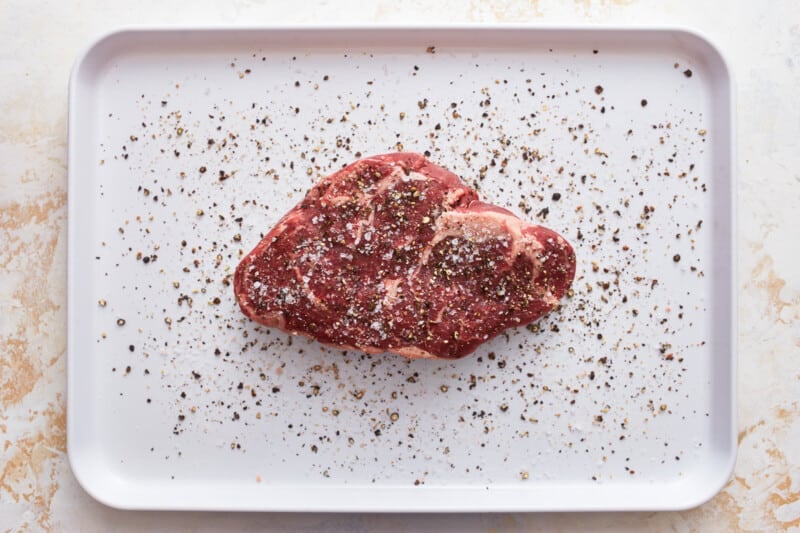 seasoned ribeye steak on a baking sheet.