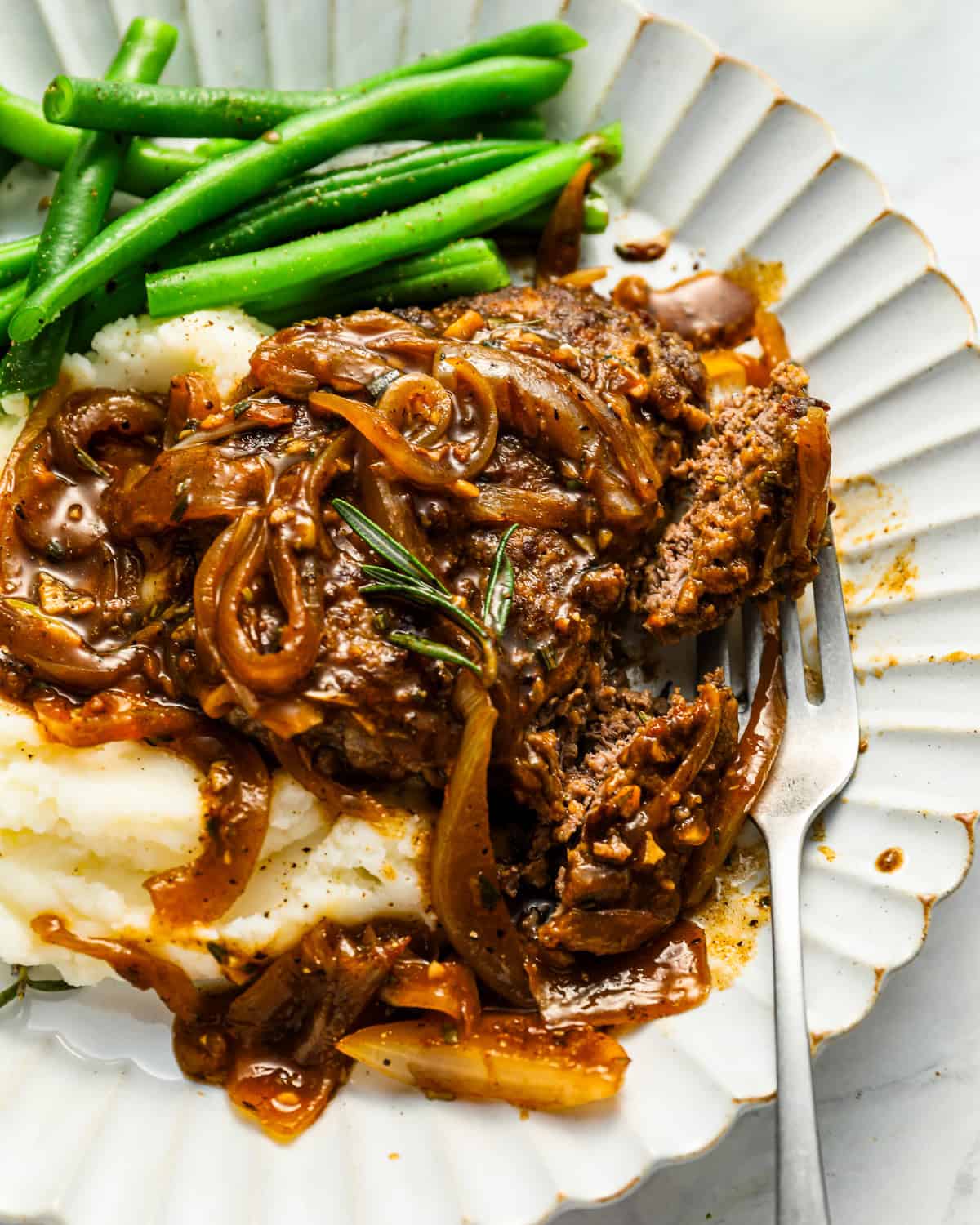 a serving of cube steak on a white plate with mashed potatoes, green beans, and a fork.