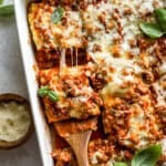 overhead view of a wooden spatula lifting a lasagna roll up from a pan.