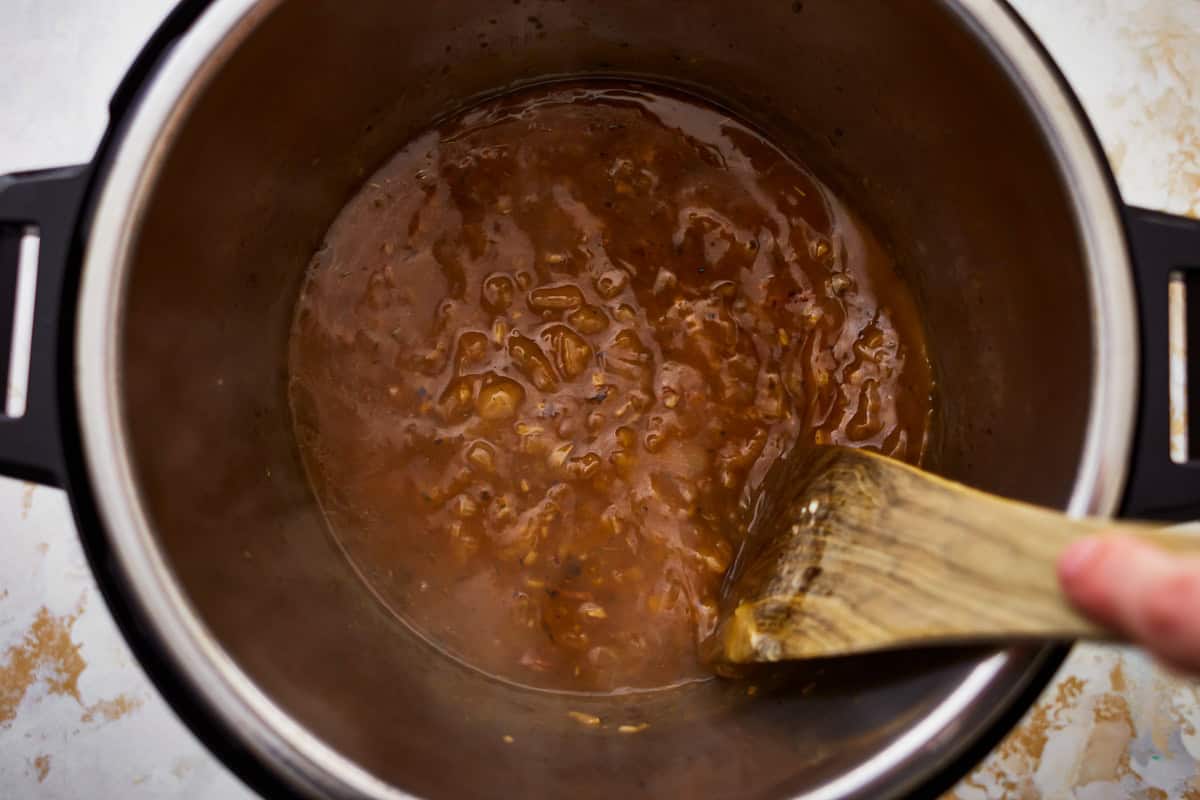 saucy onions in a pressure cooker with a wooden spoon.