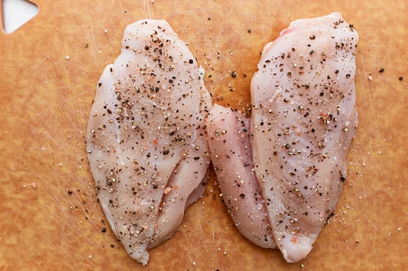 raw seasoned chicken breasts on a cutting board.