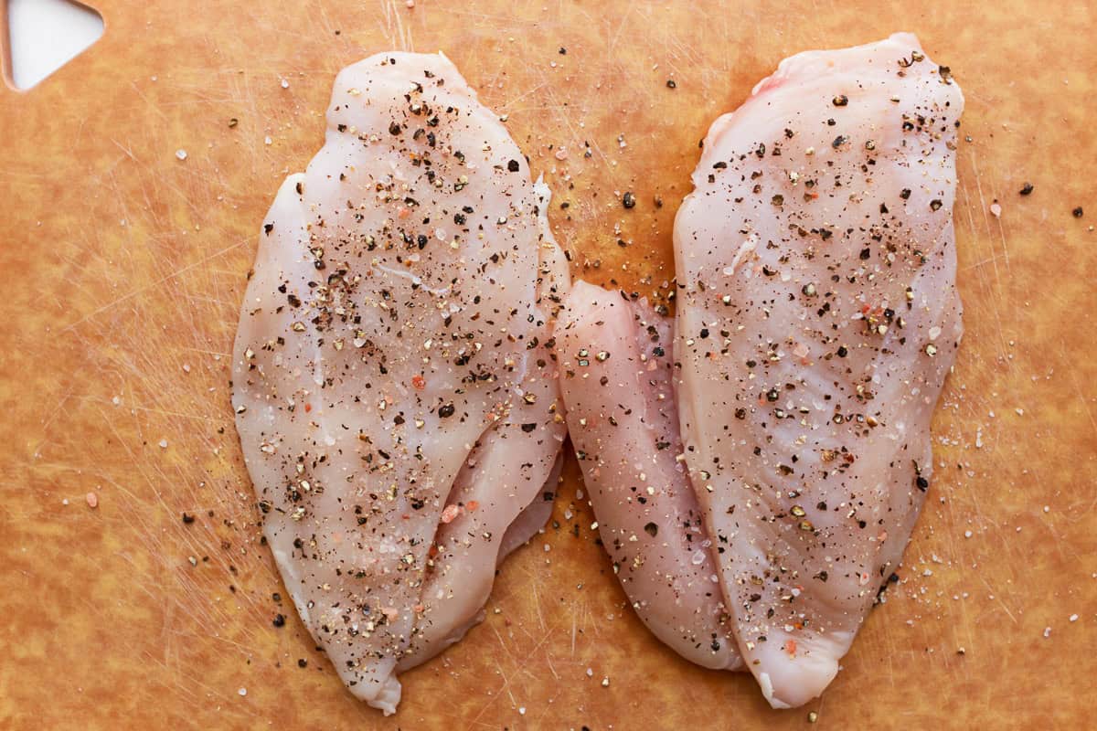 raw seasoned chicken breasts on a cutting board.