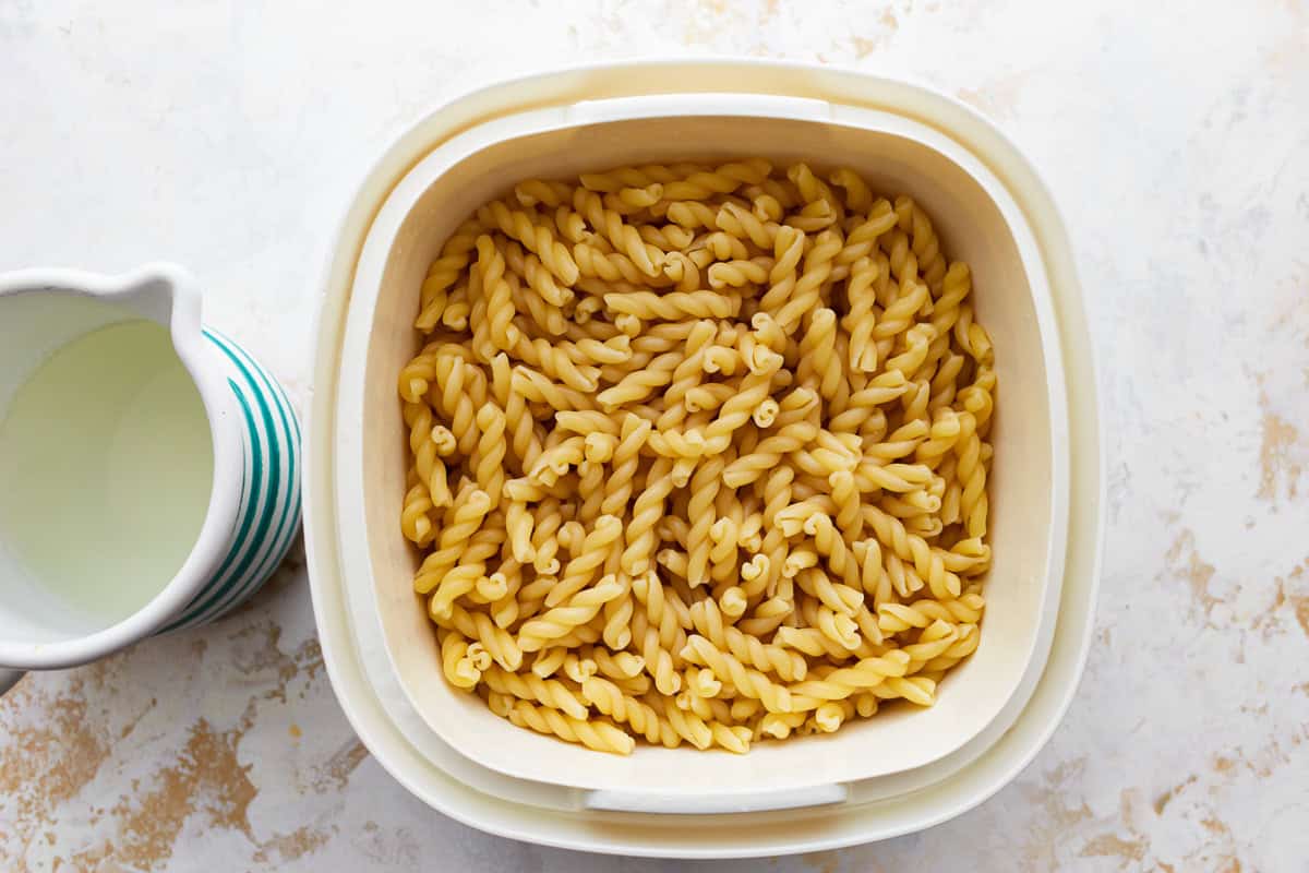 cooked pasta in a colander next to a cup of pasta water.