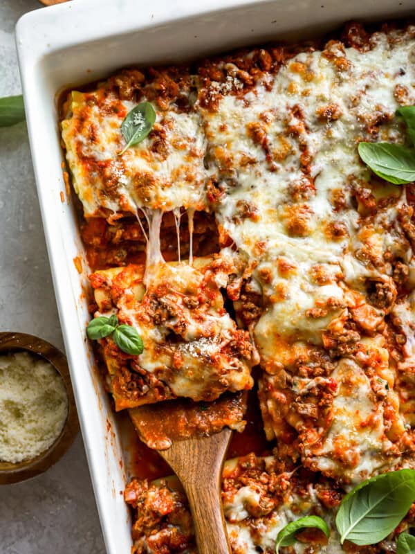 overhead view of a wooden spatula lifting a lasagna roll up from a pan.