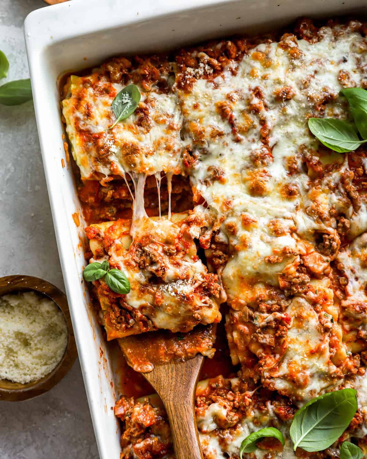 overhead view of a wooden spatula lifting a lasagna roll up from a pan.