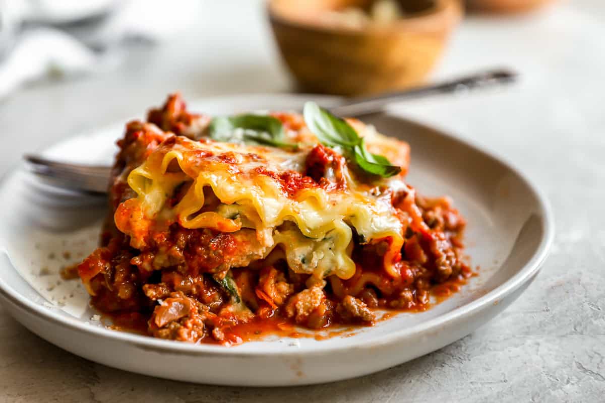 side view of a lasagna roll up on a gray plate with a fork.