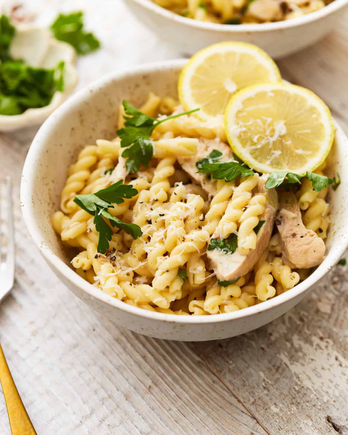 a serving of lemon chicken pasta in a bowl with lemon slices.