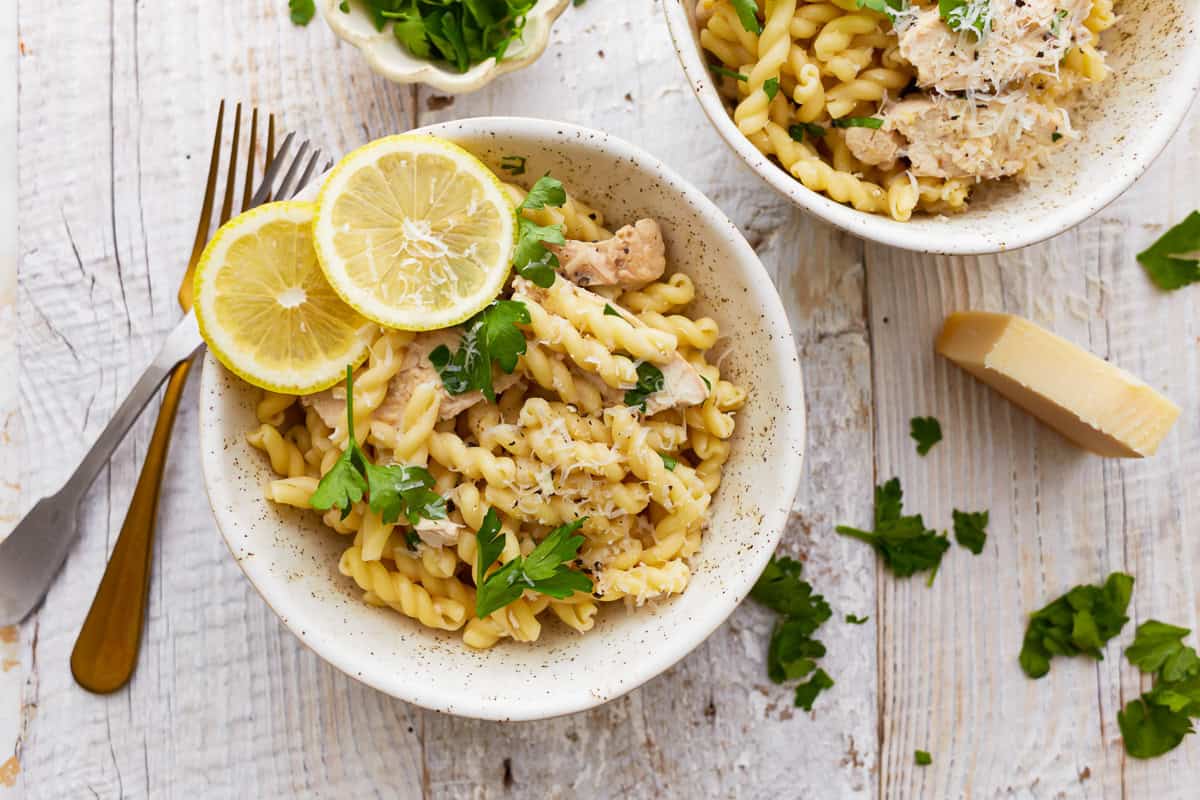 overhead view of a serving of lemon chicken pasta in a bowl with lemon slices.