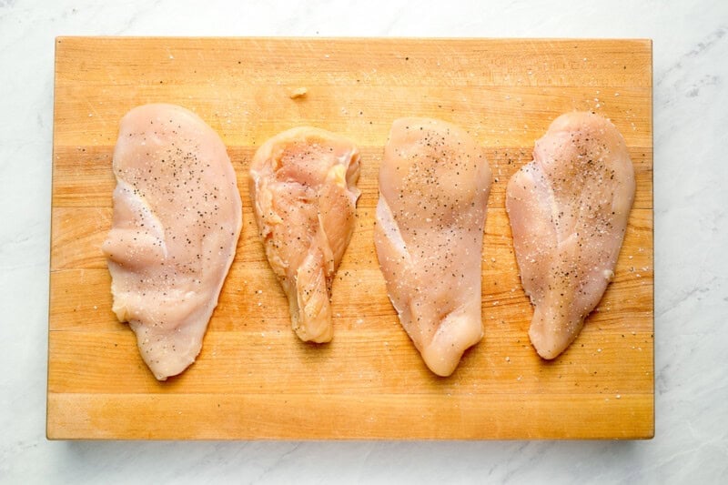 4 seasoned raw chicken breasts on a cutting board.