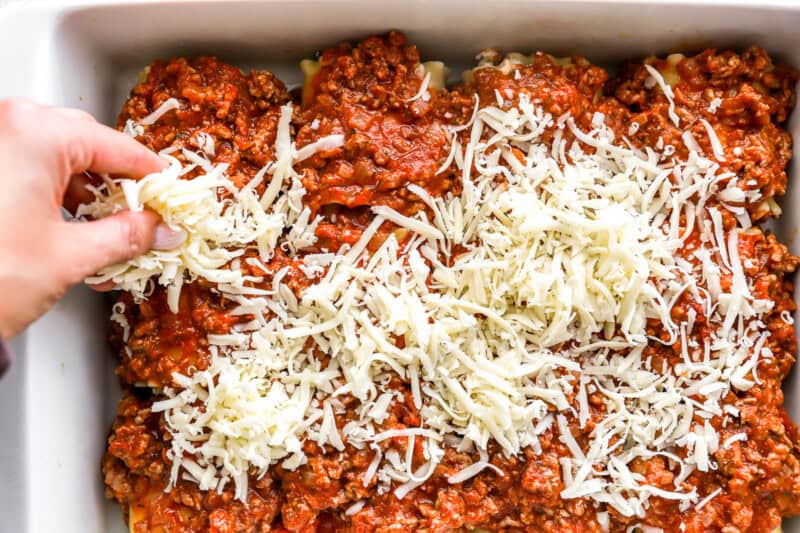 sprinkling cheese over lasagna roll ups in a baking dish.