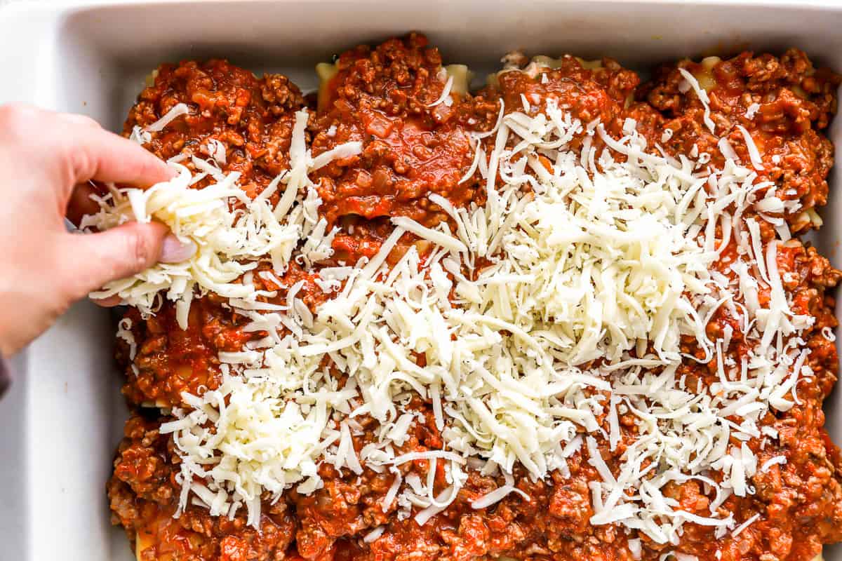 sprinkling cheese over lasagna roll ups in a baking dish.