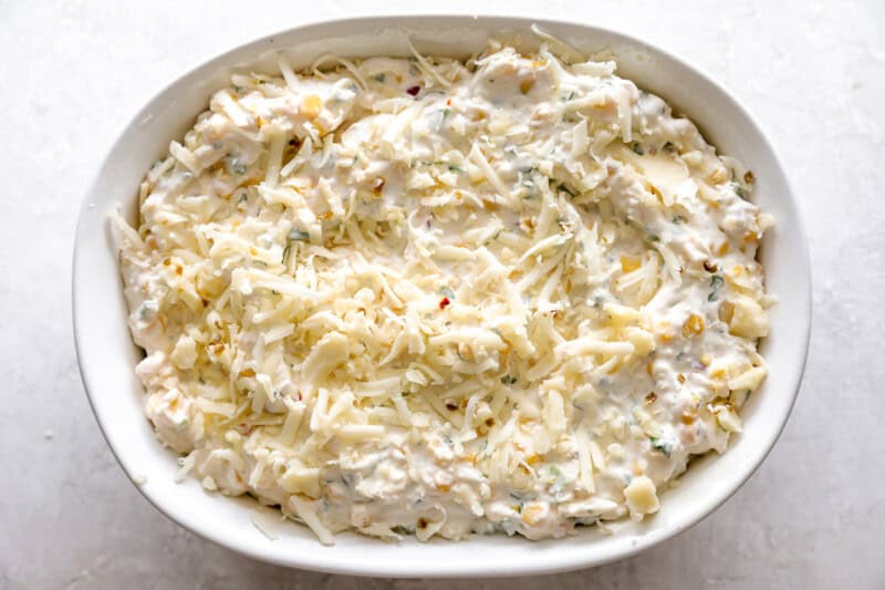 mexican street corn dip topped with cheese in an oval baking dish.