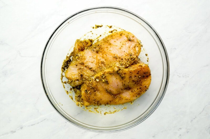 chicken breasts coated in pesto in a glass bowl.