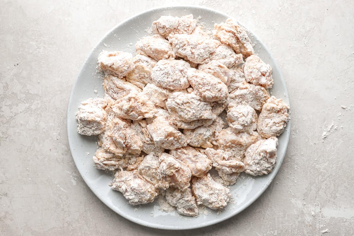 tiny pieces of chicken dredged in seasoned flour on a white plate.