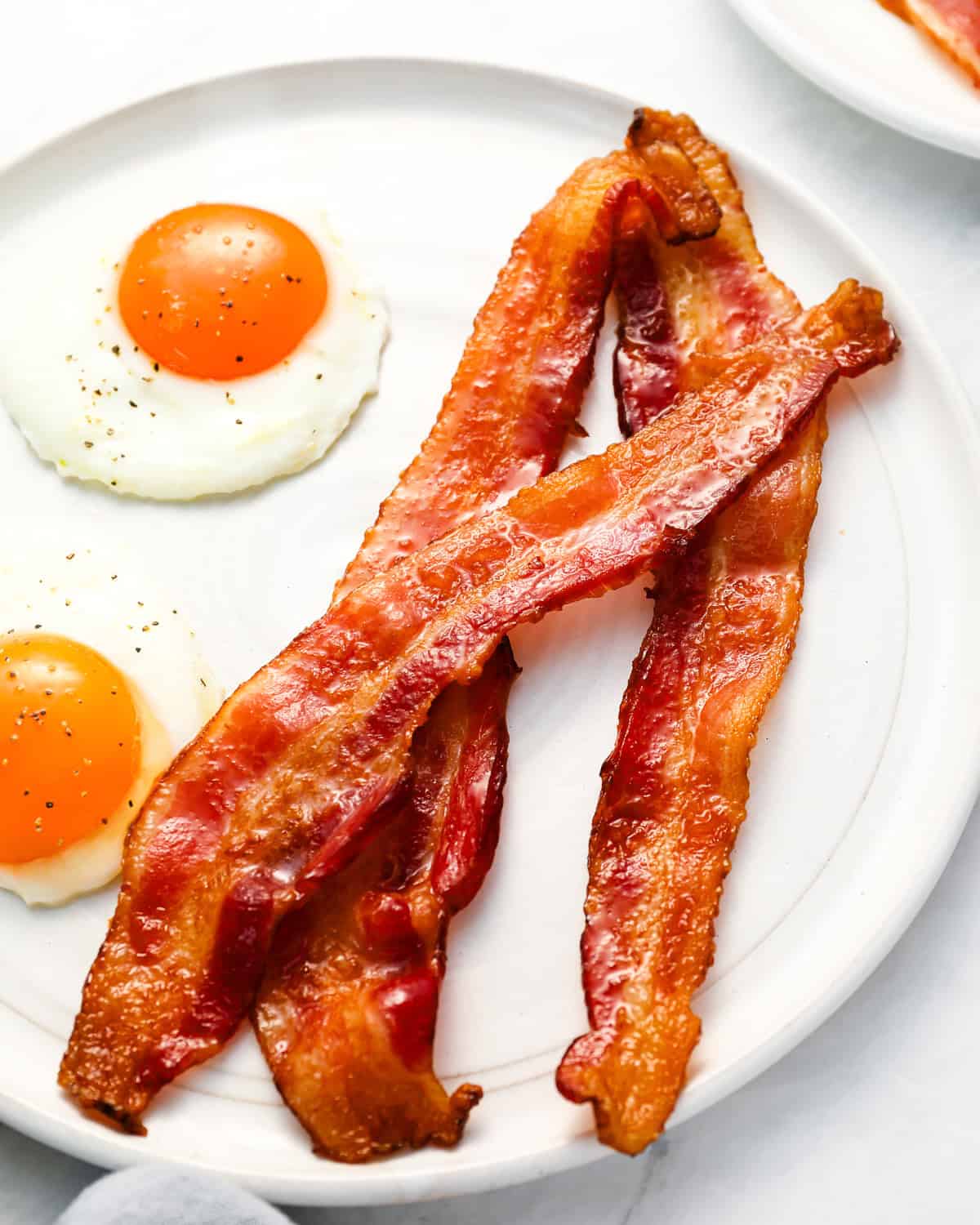 3 strips of cooked bacon and 2 fried eggs on a white plate.