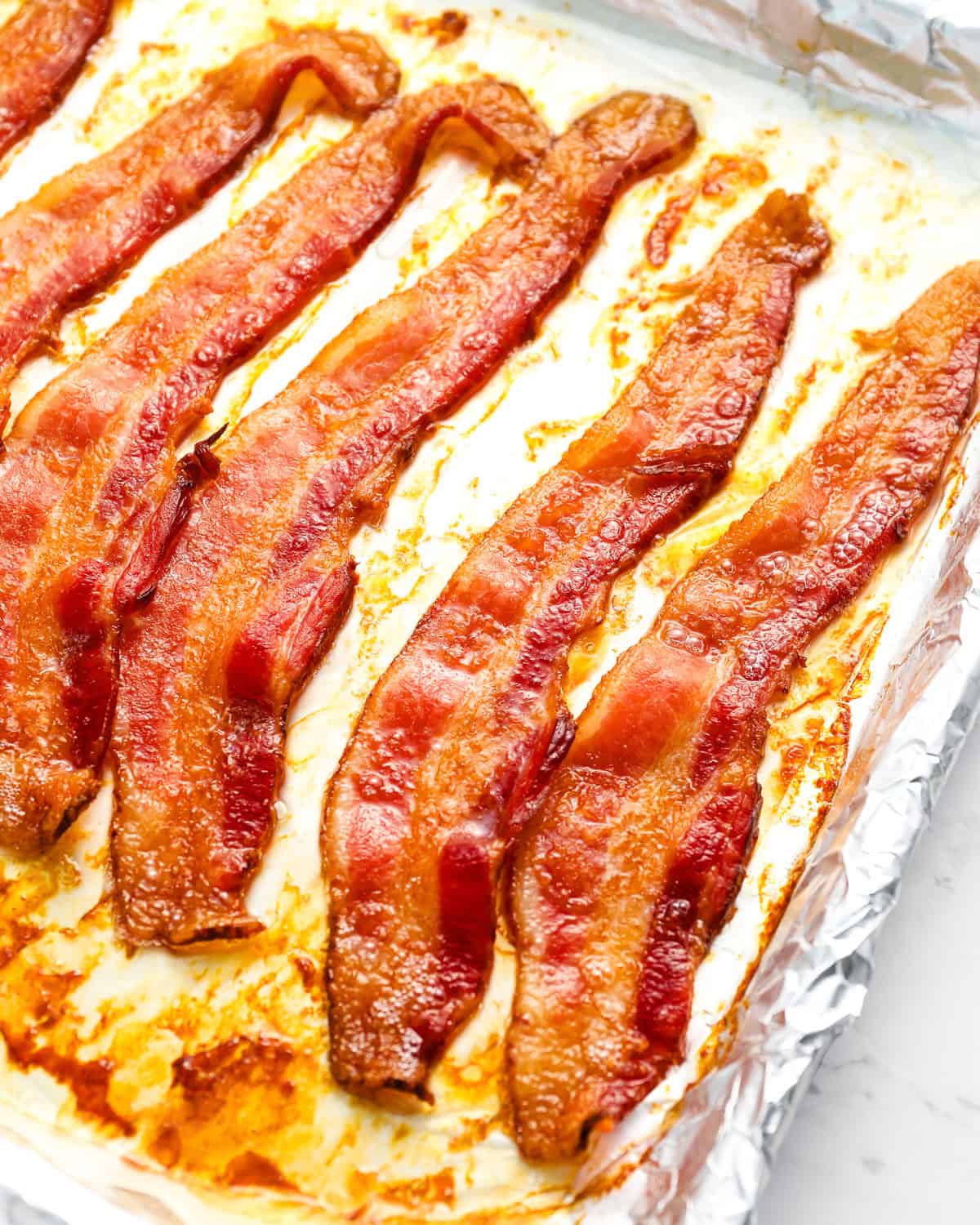 slices of cooked bacon on a foil-lined baking sheet.