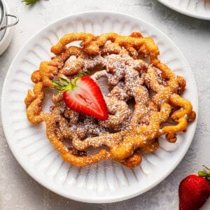 overhead view of a funnel cake with a strawberry on a white plate.