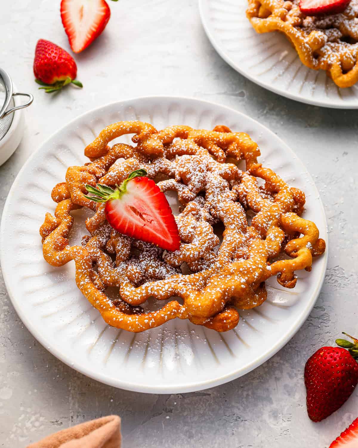 a funnel cake with a strawberry on a white plate.