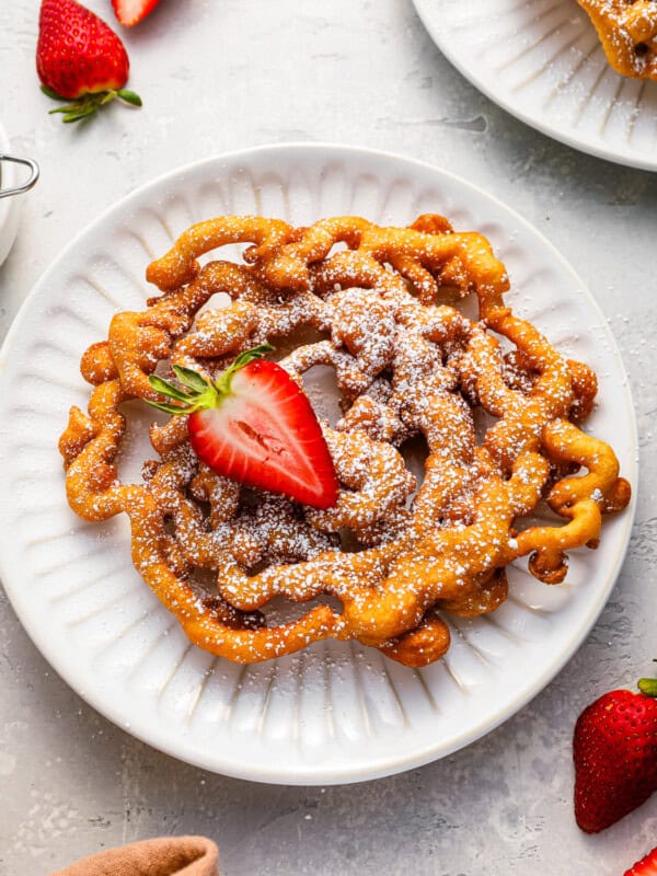 overhead view of a funnel cake with a strawberry on a white plate.