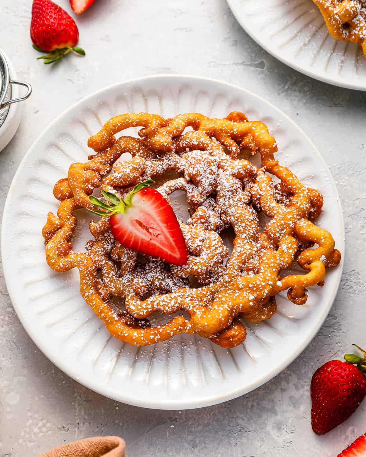 overhead view of a funnel cake with a strawberry on a white plate.