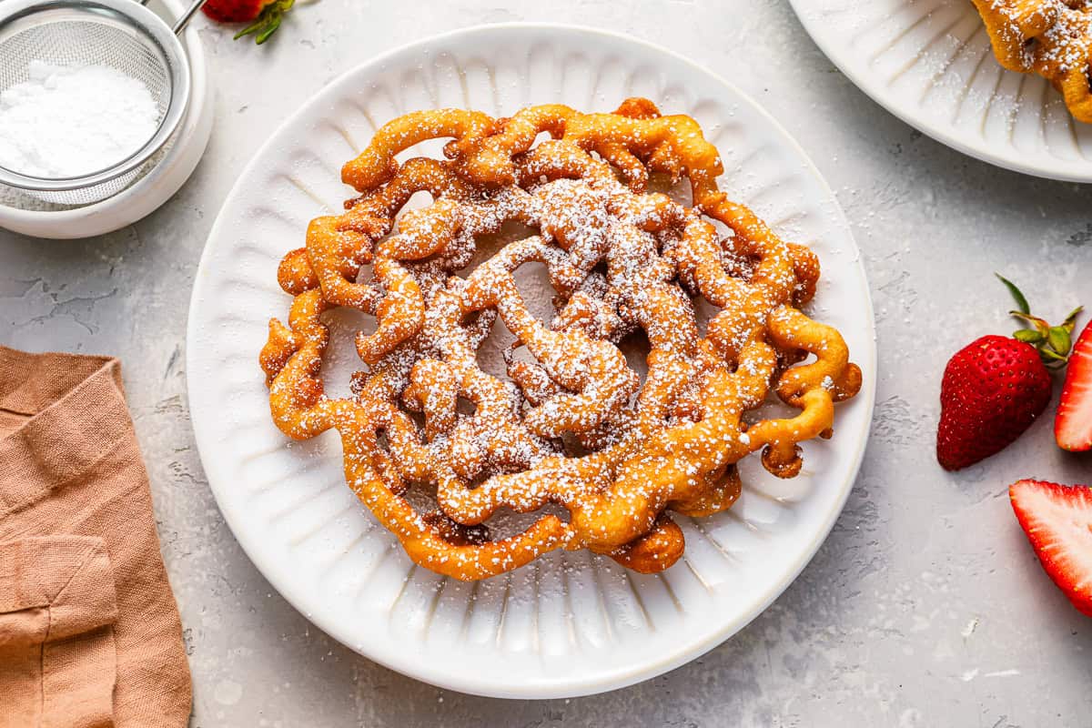a funnel cake topped with powdered sugar on a white plate.