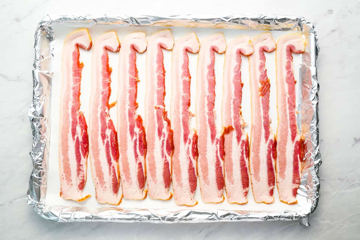 raw bacon strips on a foil-lined baking sheet.