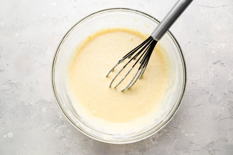 funnel cake batter in a glass bowl with a whisk.