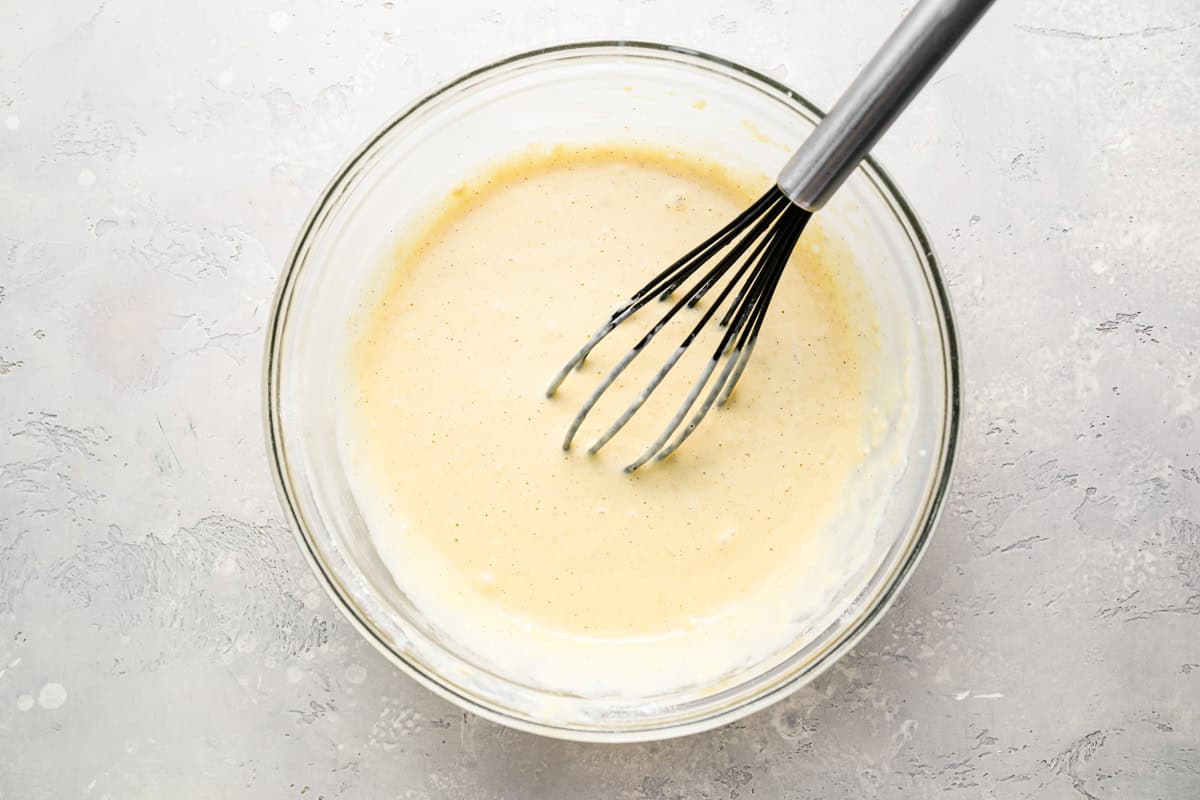 funnel cake batter in a glass bowl with a whisk.