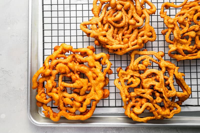 funnel cakes draining on a wire rack set in a baking sheet.