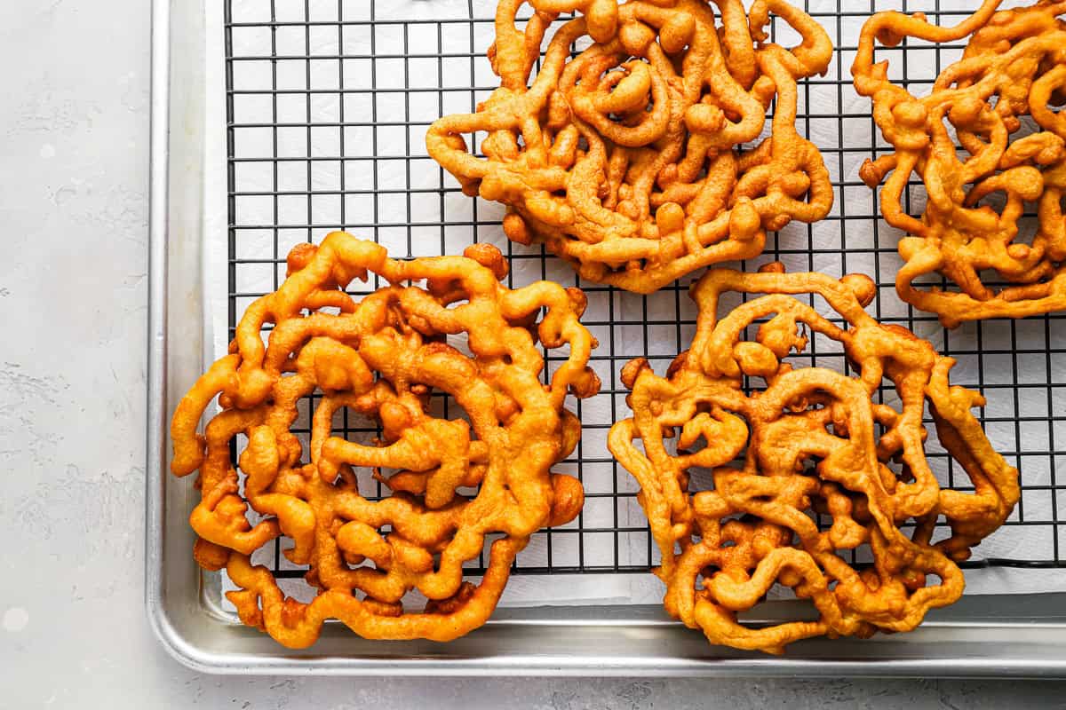 funnel cakes draining on a wire rack set in a baking sheet.