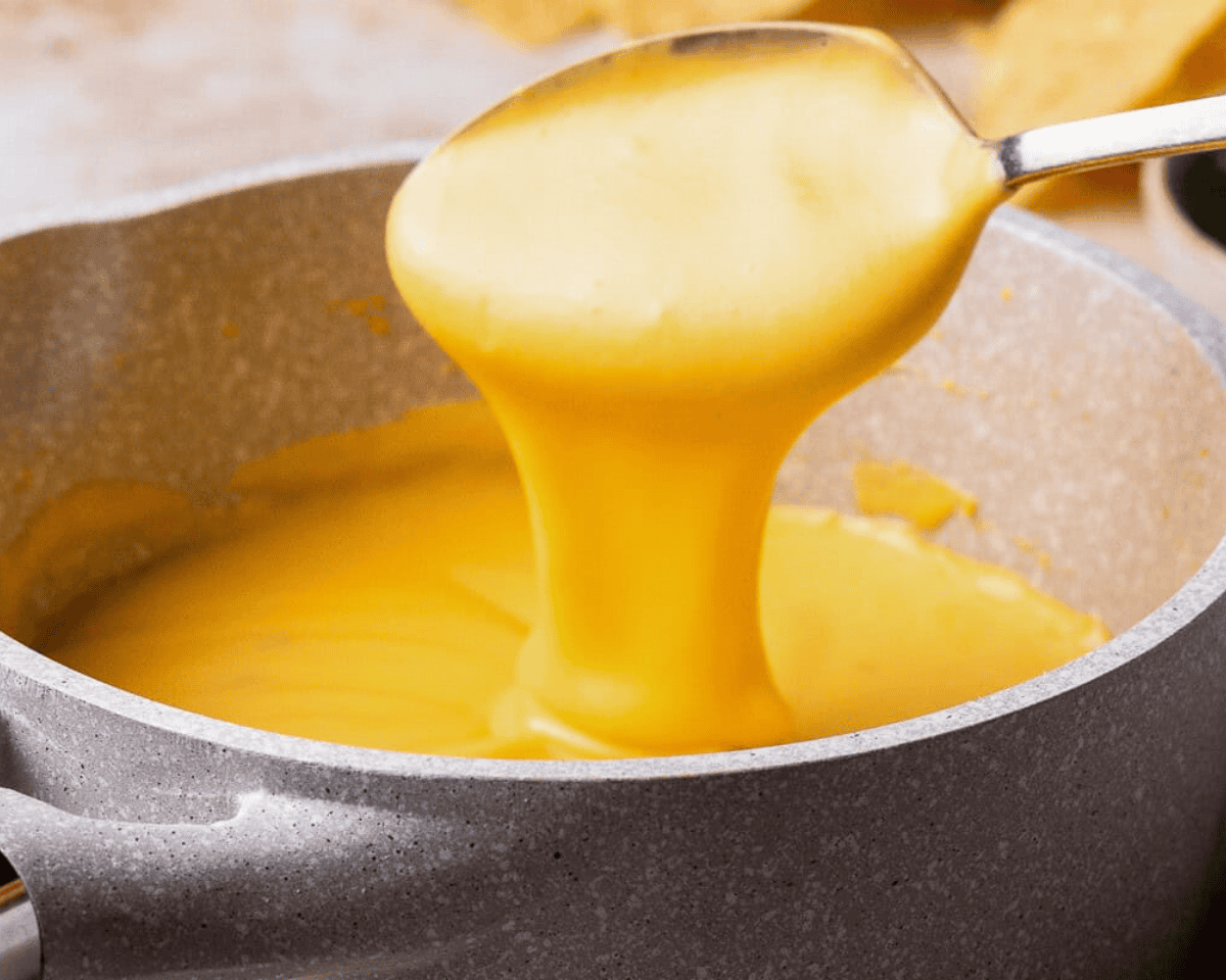 spoon dipping into a pot of cheese sauce