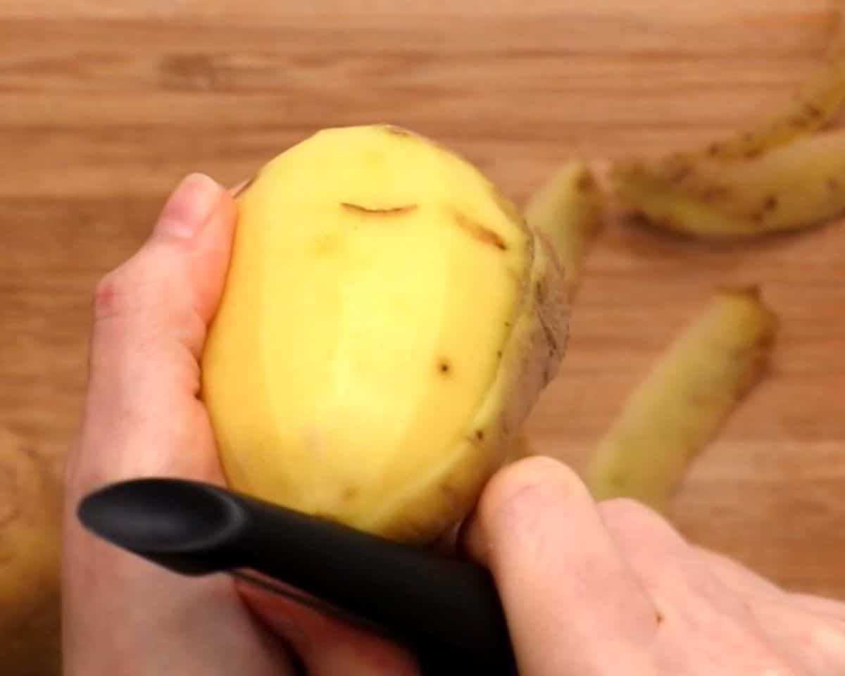 Peeling the potatoes with a potato peeler.