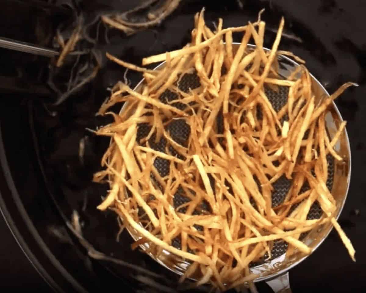 Removing the cooked fries from the hot oil with a strainer.