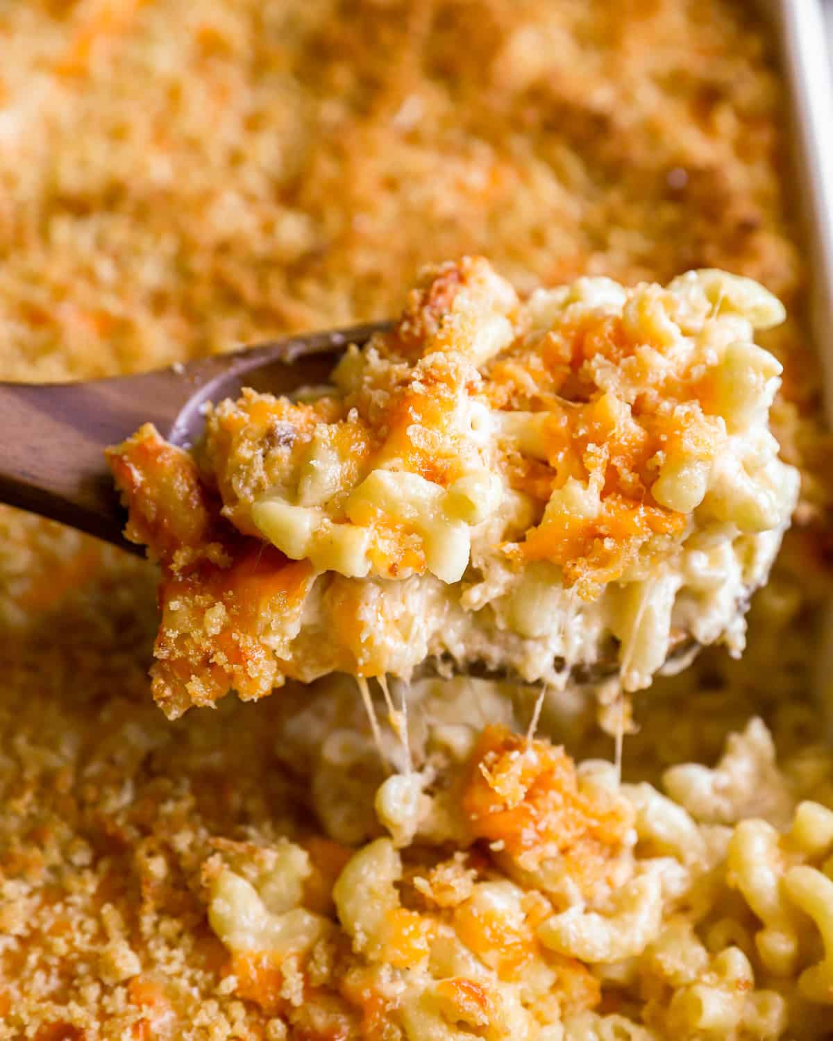 closeup view lifting a scoop of baked mac and cheese from a casserole dish with a wooden spoon.