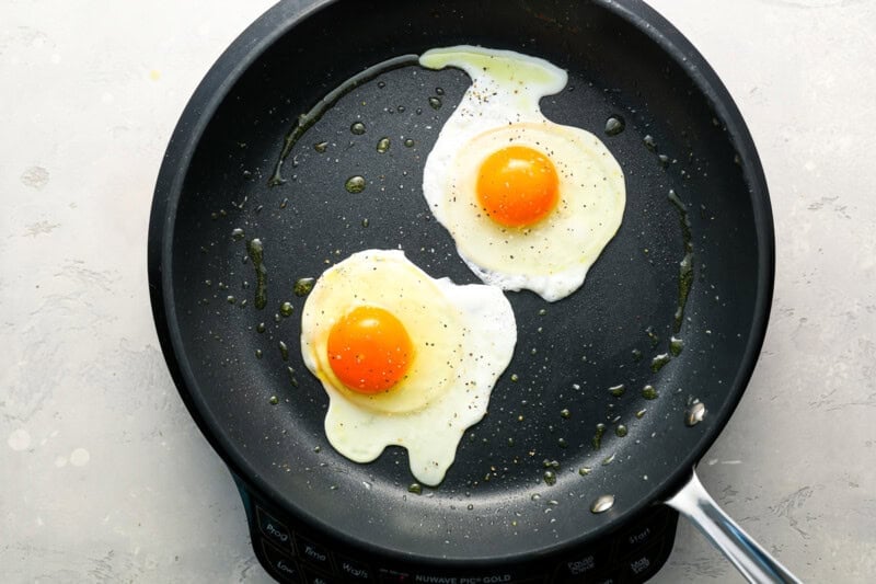 cooking 2 seasoned sunny side up eggs in a nonstick pan.